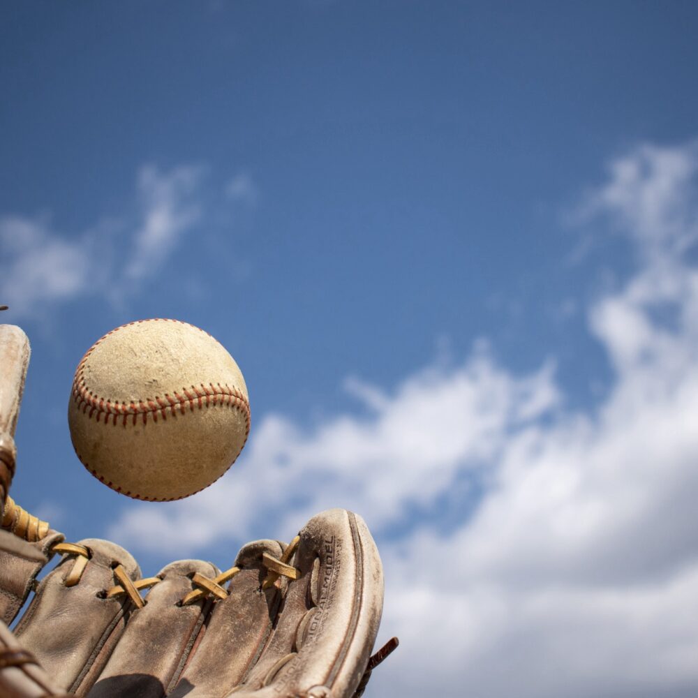 Baseball dropping into a leather glove against a blue sky — HammerZone Baseball Camp